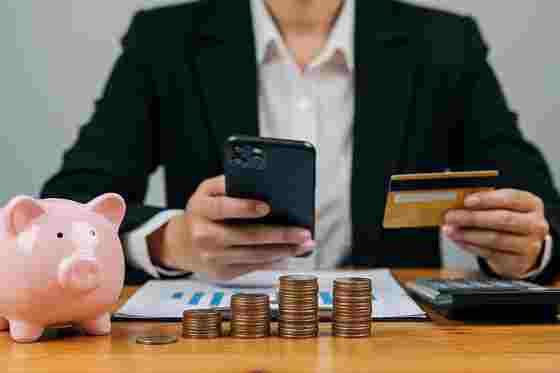 Mann mit Smartphone, Bankomatkarte, Sparschwein und Münzen