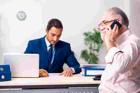 Pensionist telefoniert, Sachbearbeiter am Schreibtisch